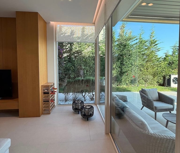 Modern interior with large glass doors opening to patio and forest view, featuring wooden partition, neutral flooring, and contemporary furniture