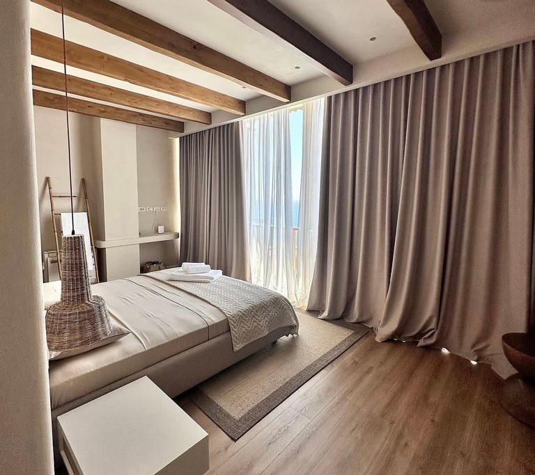 Modern bedroom with canopy bed, exposed wooden beams, floor-to-ceiling curtains, and hardwood flooring
