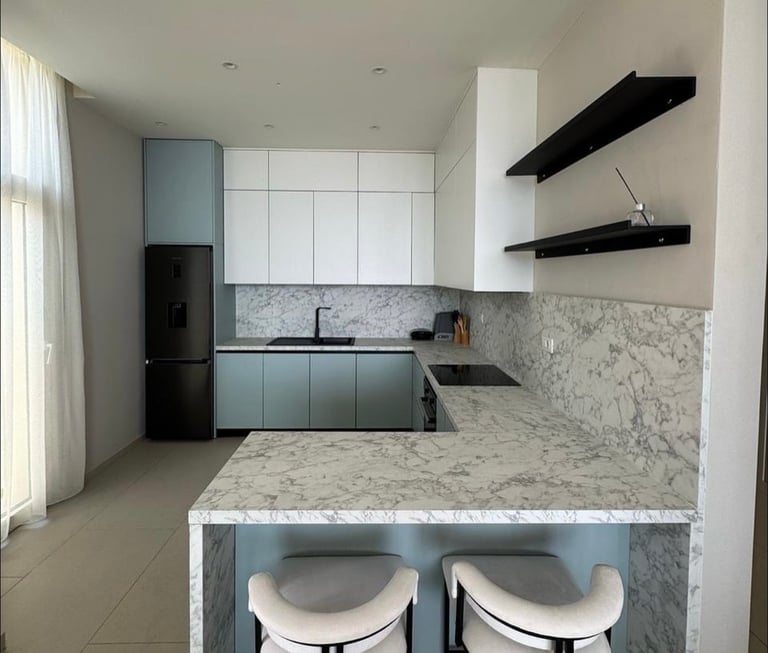 Modern kitchen with white and blue cabinetry, marble countertop, black shelves, and two bar stools at the island.