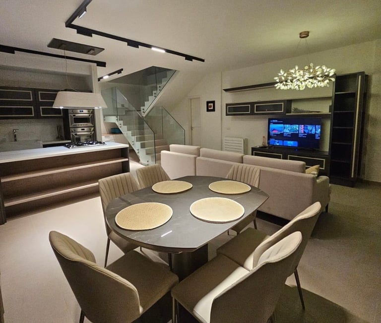 Modern open-plan living space with dining table set for four, cream sofa, kitchen with bar counter, and staircase in contemporary home