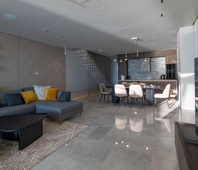 Modern open-concept apartment interior with blue sectional sofa, dining area, and kitchen visible in contemporary design