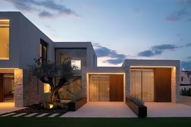 Modern minimalist house exterior at dusk with illuminated windows, dark gray facade, and integrated garage at twilight