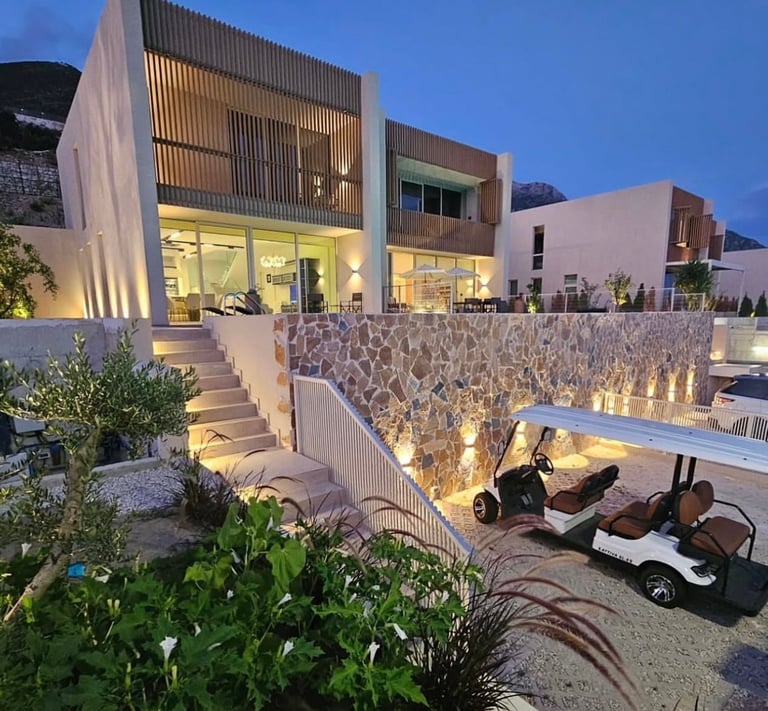 Modern luxury resort villa at twilight with illuminated stone walls, manicured landscaping, and golf carts in courtyard