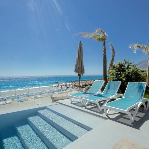 Beachfront lounge area with turquoise sun loungers overlooking Mediterranean sea