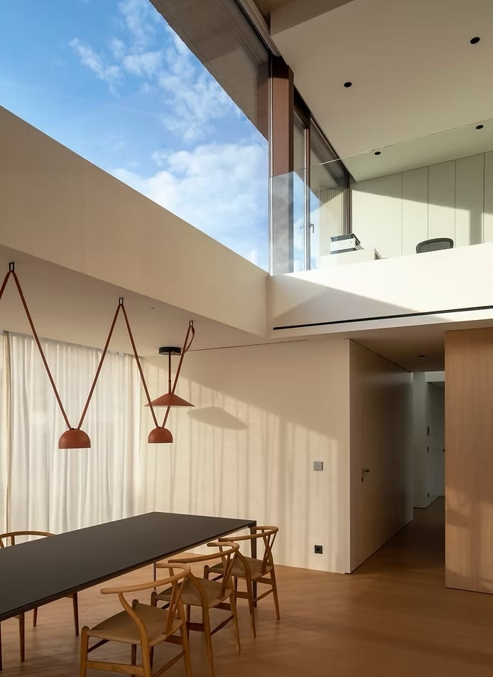 Modern minimalist dining room with skylight, black table, wooden chairs, and hanging pendant lights