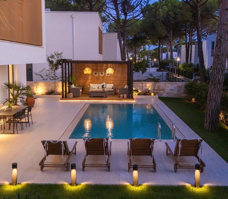 Modern backyard with illuminated swimming pool, lounge chairs, lit ambient garden lighting, and contemporary wooden pool house at dusk.