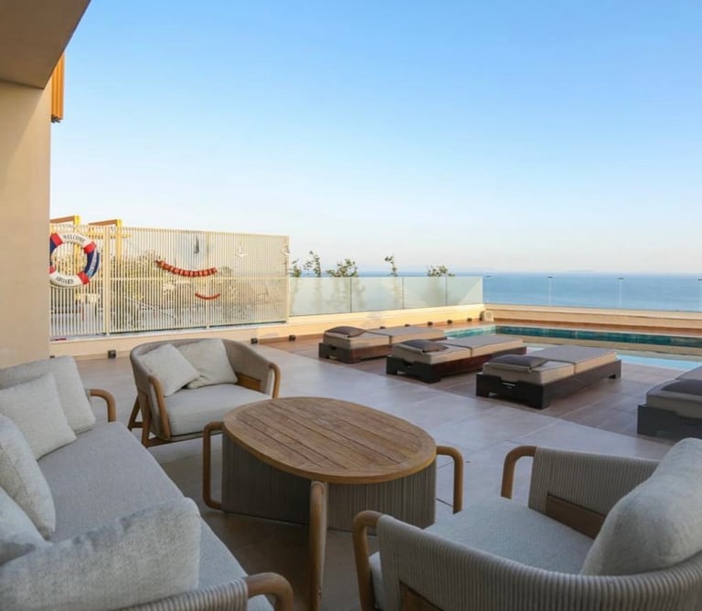 Modern terrace with lounge seating, wooden table, and swimming pool overlooking calm blue sea
