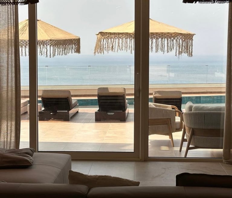 Luxury beachfront resort balcony with lounge chairs, decorative umbrellas, and ocean view through glass doors