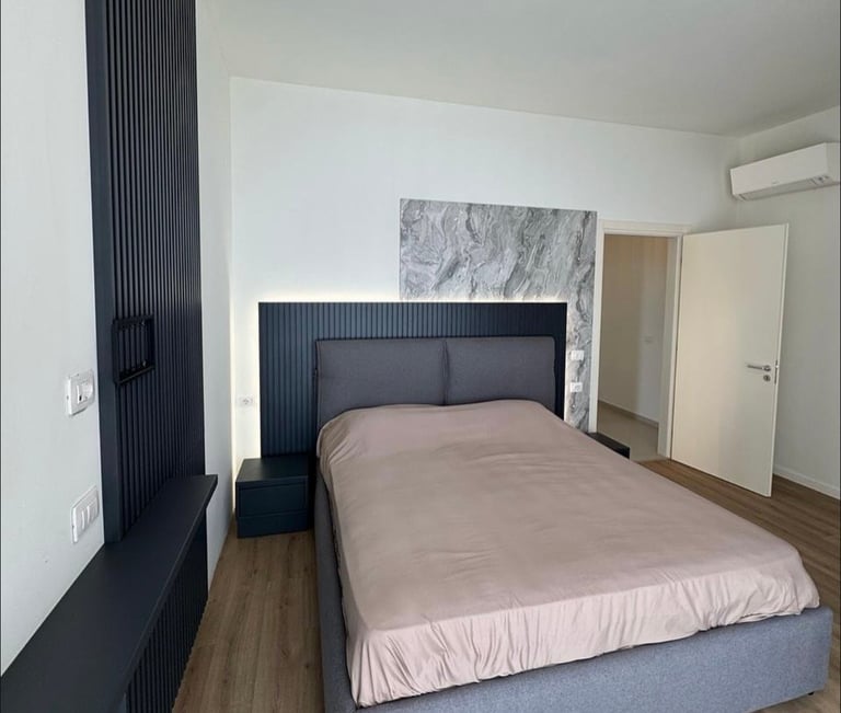 Modern bedroom with queen bed, black headboard, wood flooring, white walls, and marble artwork above headboard