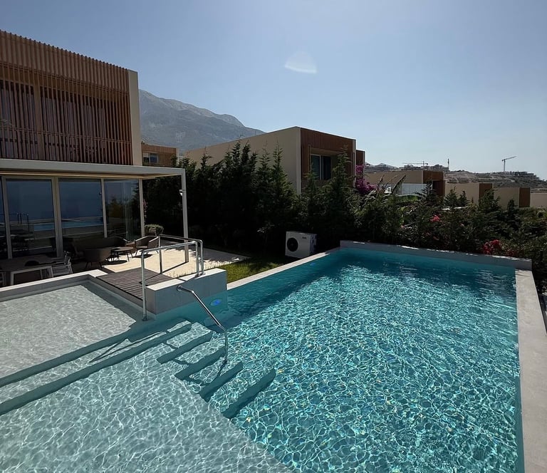 Modern luxury home with turquoise swimming pool, wooden deck lounge chairs, and mountain views on sunny day