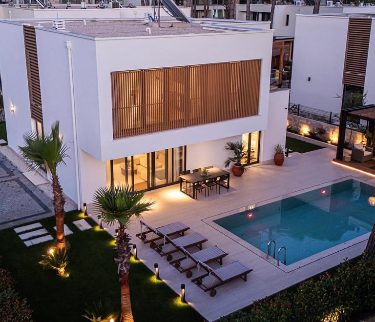 Modern white house with swimming pool, lounge chairs, and illuminated outdoor patio area at dusk