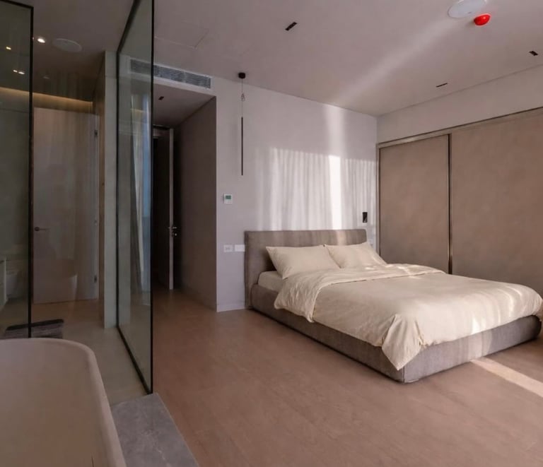 Modern minimalist bedroom with king bed, glass shower enclosure, and neutral color palette