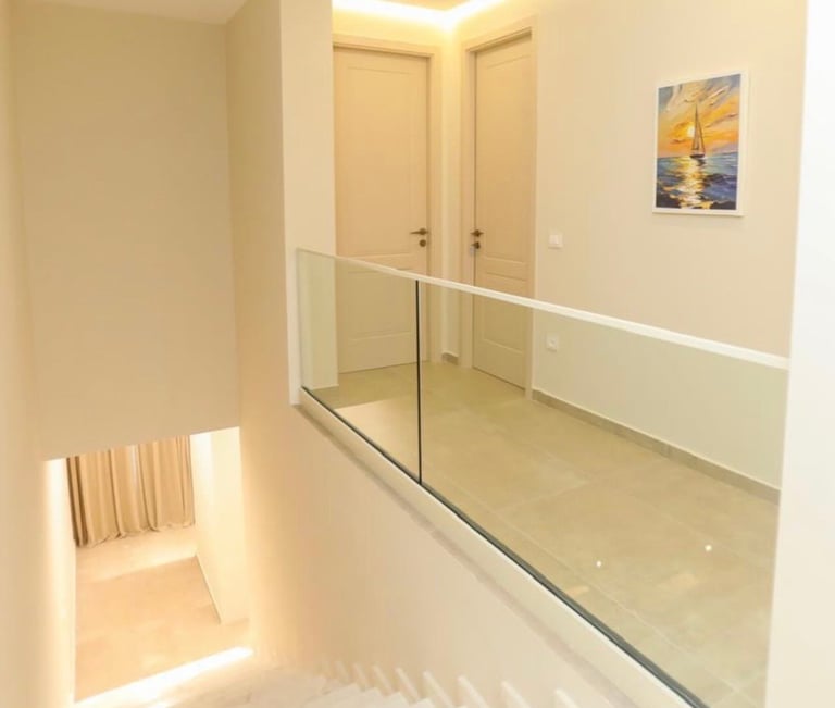 Modern bathroom hallway with glass shower enclosure, beige tile flooring, cream walls, towel rack, and nautical artwork
