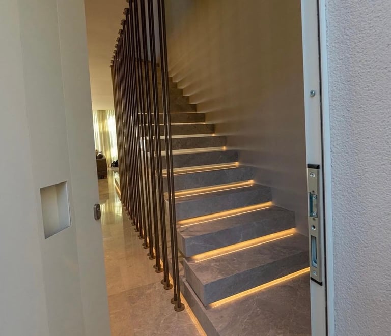 Modern staircase with warm LED lighting under steps, metal railings, and white walls in a contemporary interior space.